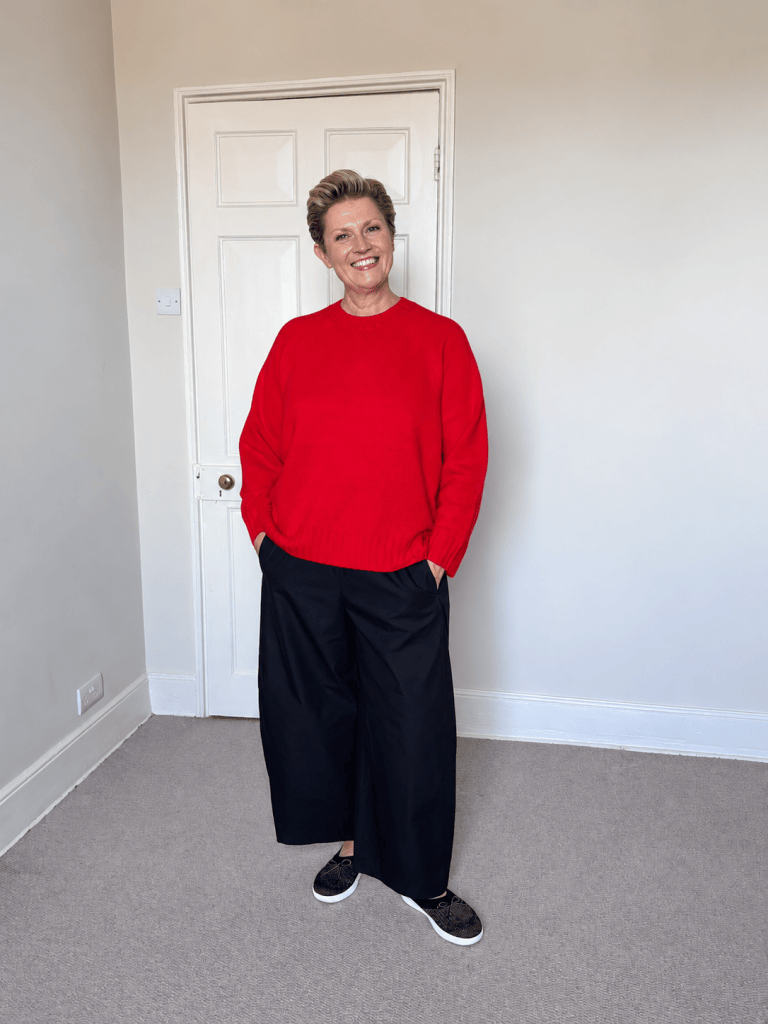 Susy wearing black COS barrel-leg trousers with a bright red jumper